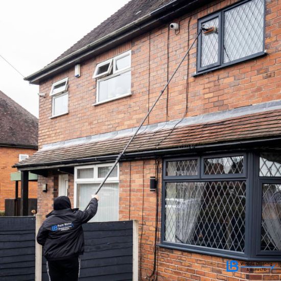 residential window cleaning showing a window cleaner using a pole watering system to clean the upstairs window of a house